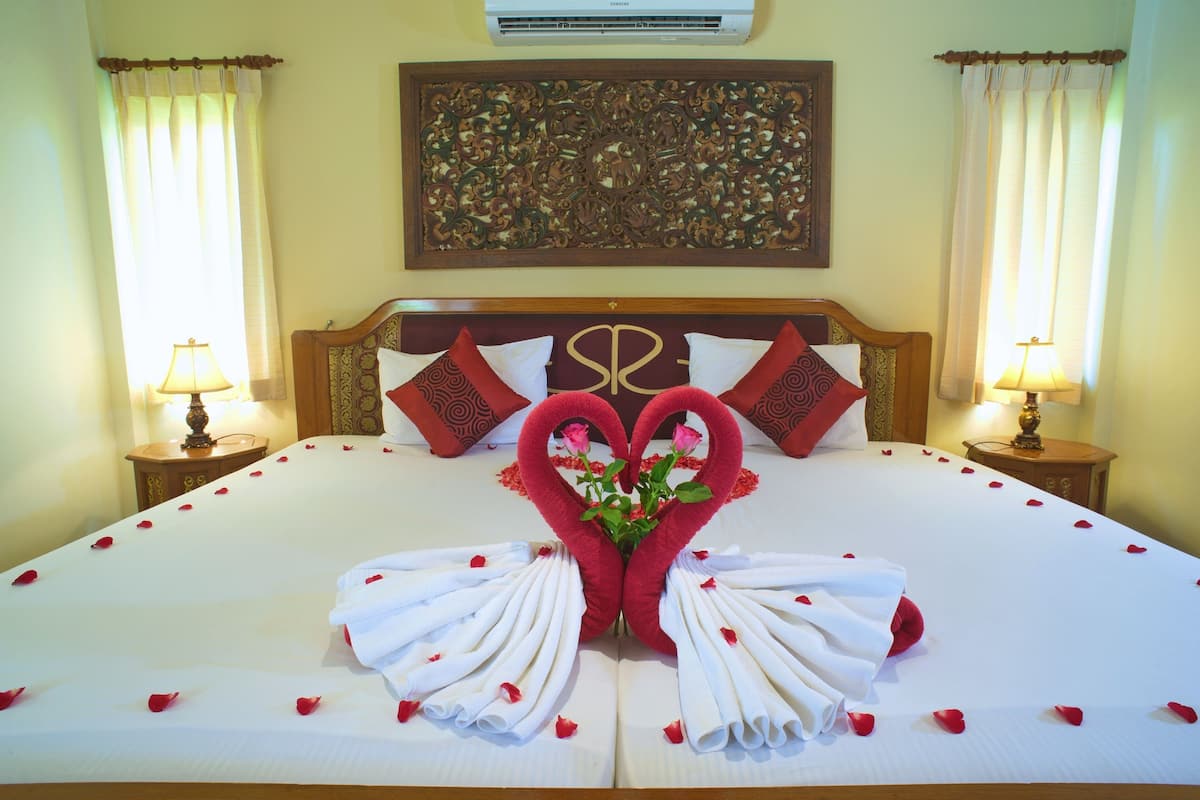 Quarto de hotel com uma cama grande, almofadas decorativas, uma obra de arte na parede e um arranjo floral.