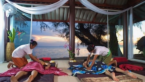 A room with a view of the sea, a fan, and two people performing a massage.