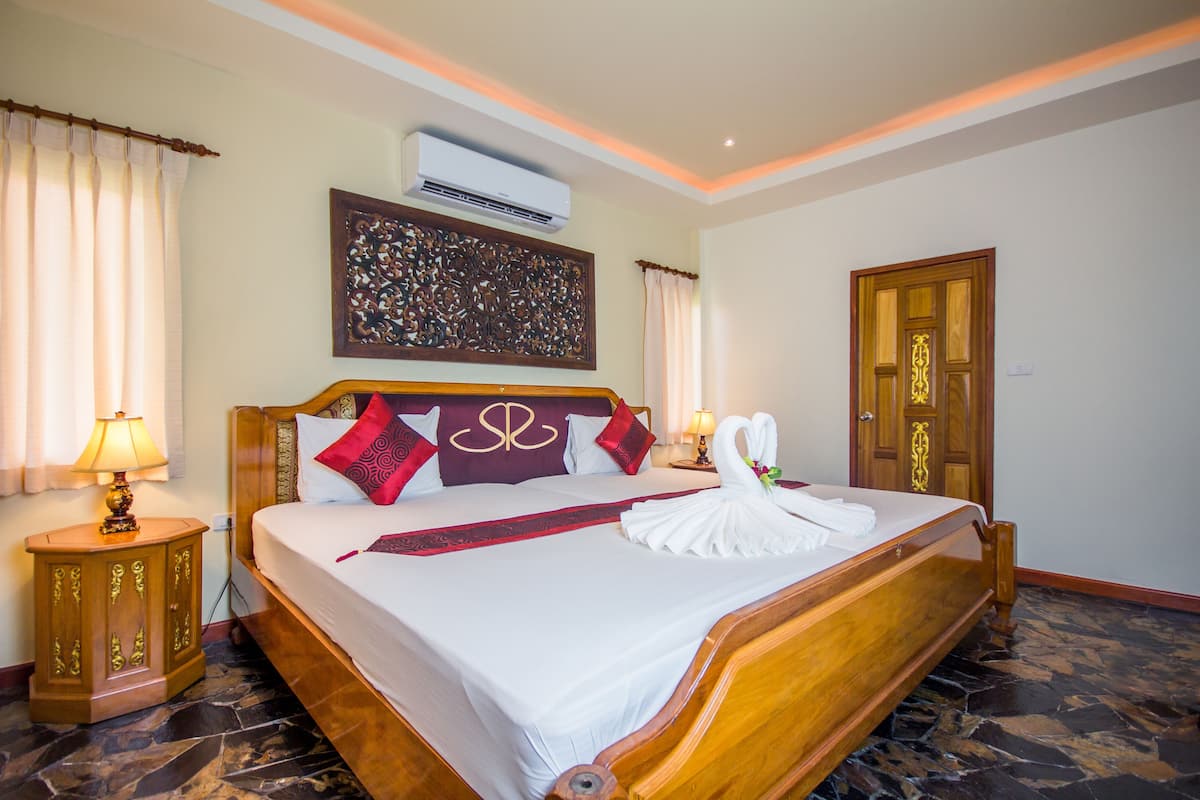 Quarto de hotel com uma cama grande, cabeceira de madeira, painel decorativo na parede, unidade de ar condicionado e porta com design detalhado.