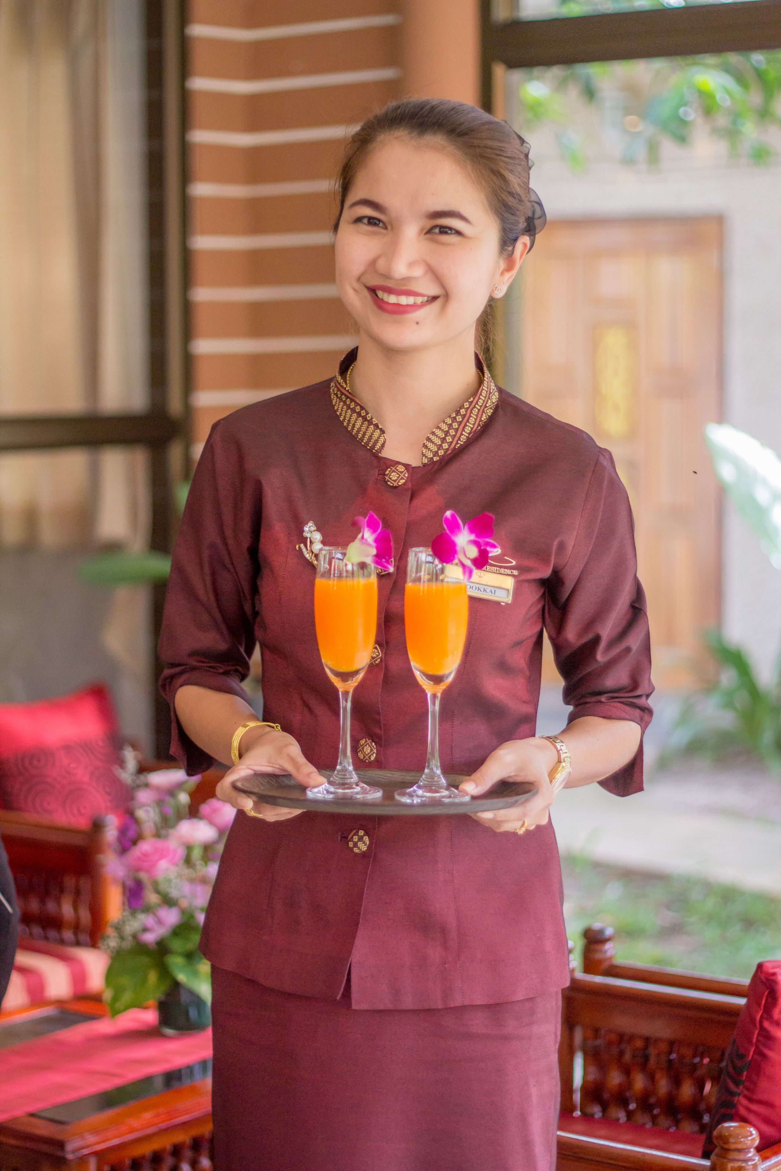 Eine Person in einer bordeauxfarbenen Uniform hält ein Tablett mit zwei Gläsern Orangensaft.