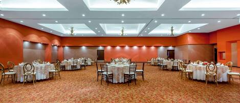 A large banquet hall with multiple round tables set for dining, equipped with chairs and table settings.