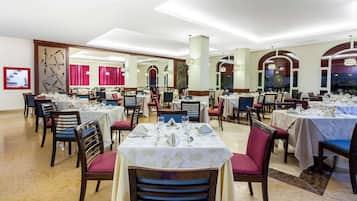 Un restaurante con varias mesas preparadas para comer, que cuenta con una decoración moderna con candelabros y ventanas arqueadas.