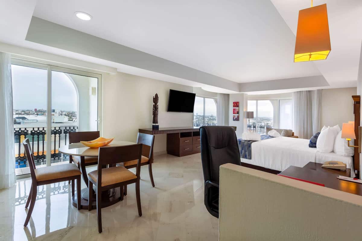 A hotel room with a balcony, a dining area, a bed, and a desk with a TV.