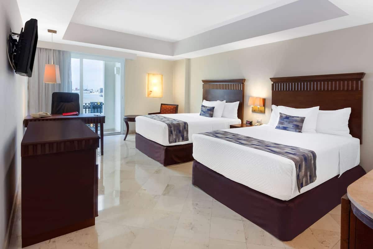 A hotel room with two beds, a desk, a TV, and a large window with a view.