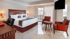 A hotel room with a bed, a desk, a chair, a TV, and a balcony with curtains. - Ramada Plaza by Wyndham Veracruz Boca del Rio (Boca del Río)