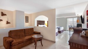 A modern living room with a brown sofa, a small round table, and a TV mounted on the wall. - Ramada Plaza by Wyndham Veracruz Boca del Rio (Boca del Río)