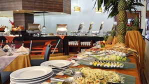 A buffet setup with various dishes, including salads, sushi, and other prepared foods, arranged on a long table with plates and utensils. - Ramada Plaza by Wyndham Veracruz Boca del Rio (Boca del Río)