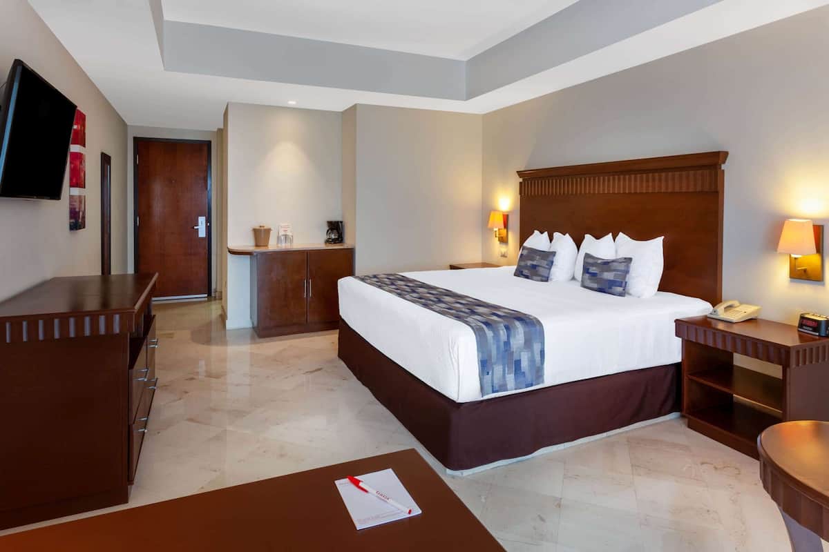 A hotel room with a large bed, bedside tables, a desk, a TV, and a bathroom.