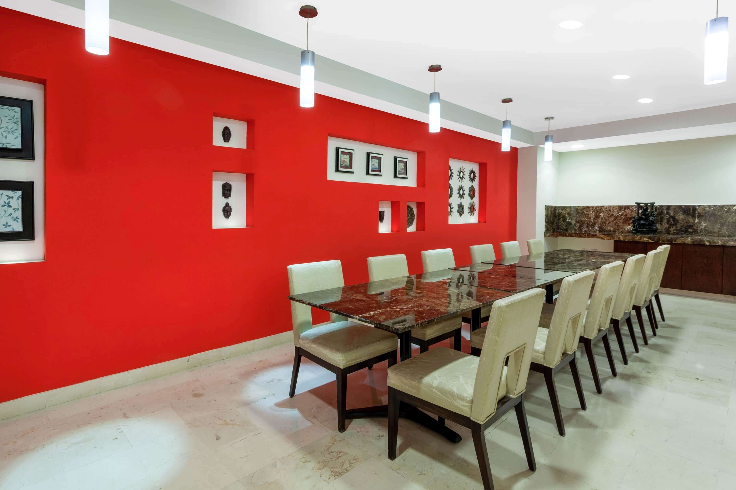Una sala conferenze con tavolo in vetro, sedie beige, una parete di fondo rossa e quadri appesi.