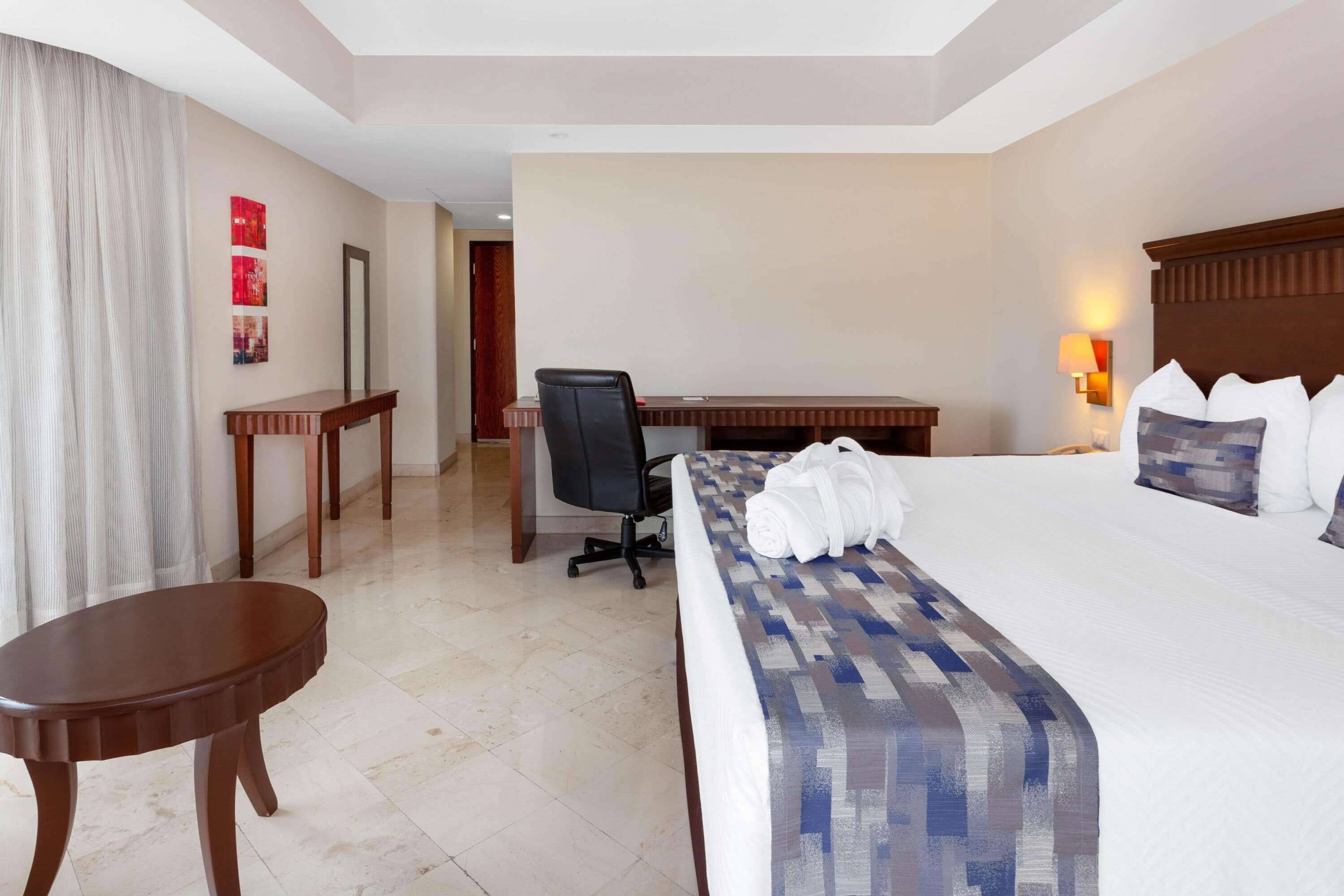 Una habitación de hotel con una cama grande, un escritorio, una silla y una mesita.
