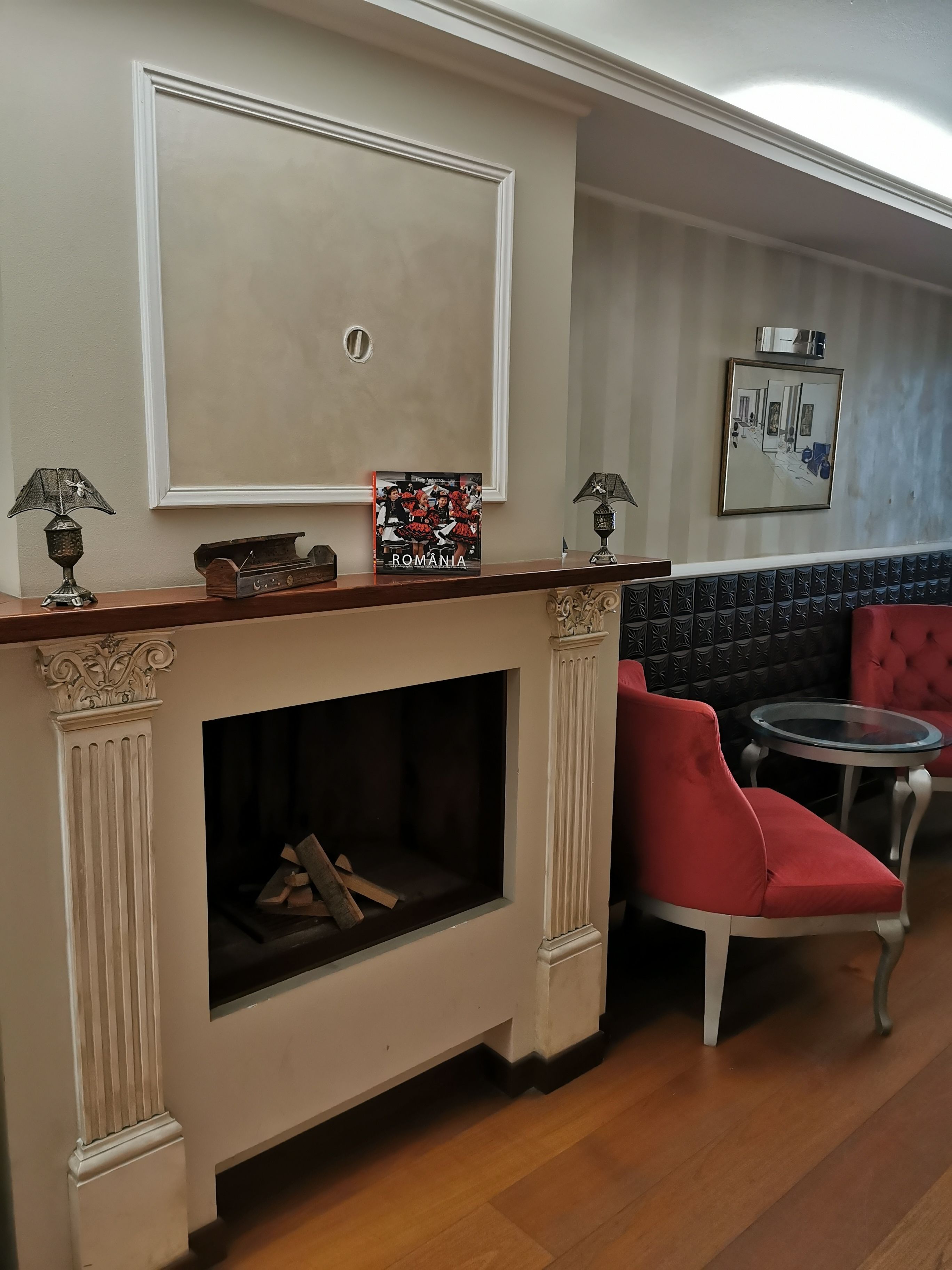 A cozy room with a fireplace, a framed picture of Romania, and a red upholstered chair.