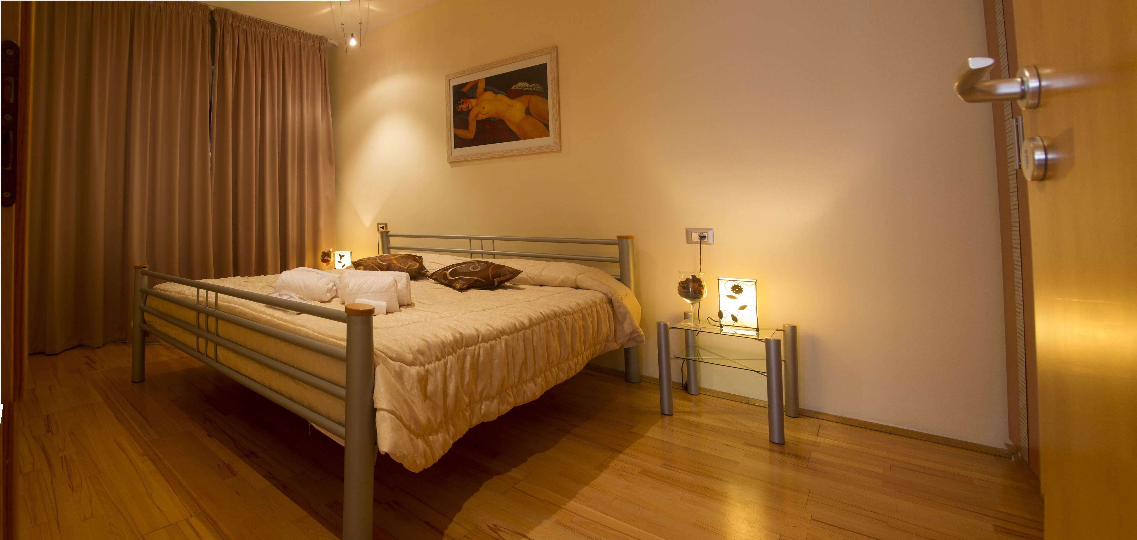 A neatly arranged bedroom with a bed, bedside tables, a lamp, and a painting on the wall.