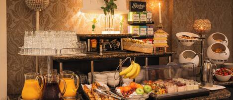 A buffet setup with various food items and beverages, including fruits, breads, and juices.
