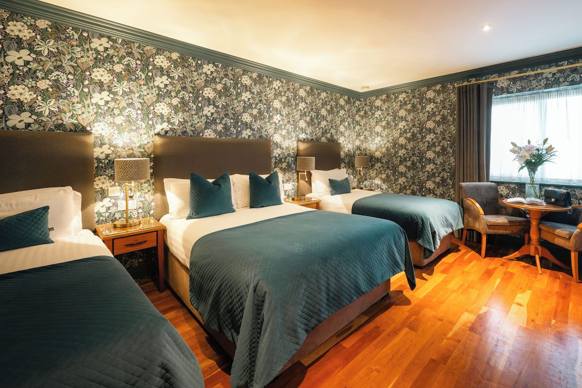 Una habitación de hotel con dos camas, una zona de estar con una silla y una mesa, y una ventana con cortinas.
