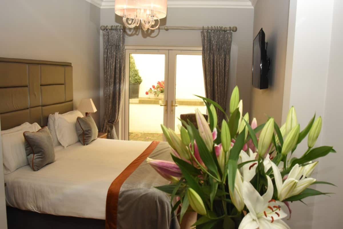 Habitación de hotel con cama, cortinas, un candelabro, un televisor y un ramo de flores.