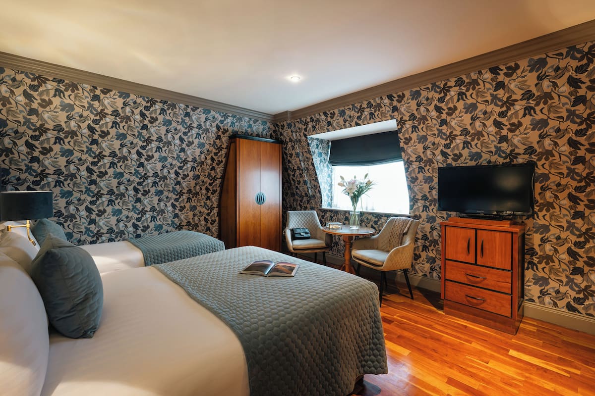 Habitación de hotel con dos camas, televisión, escritorio y ventana con vistas.