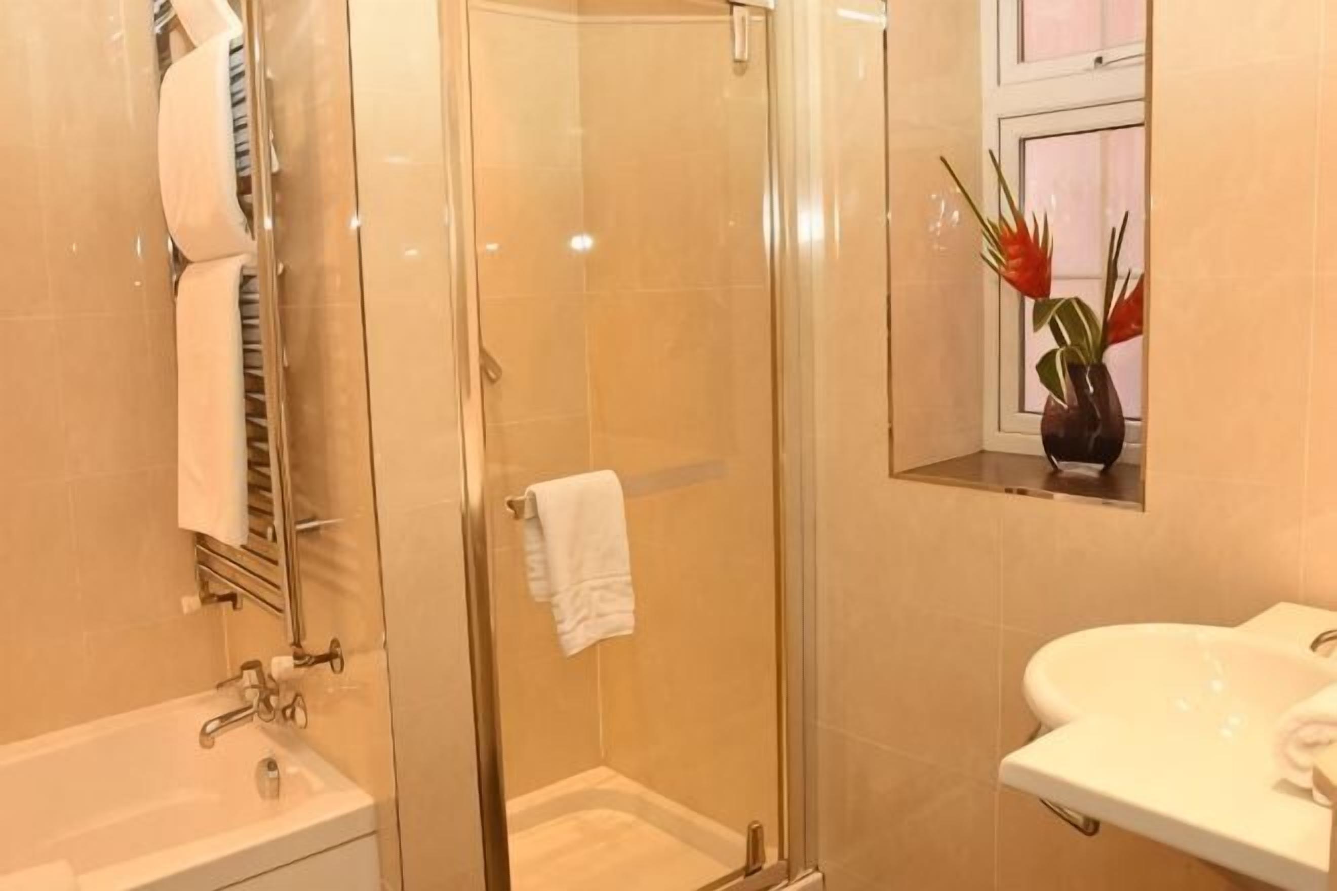 Une salle de bain avec une douche à parois de verre, un lavabo et une fenêtre agrémentée d’un vase de fleurs.