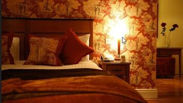 Ein Schlafzimmer mit einem Bett, einem Nachttisch, einer Lampe und blumigem Wandpapier.