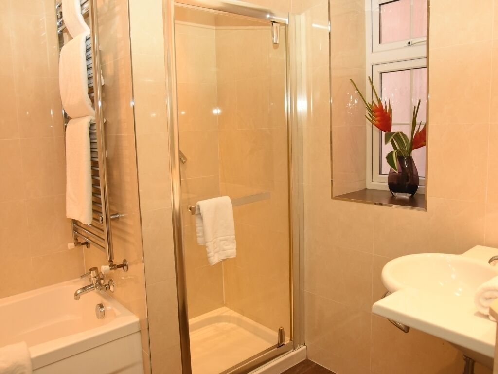 A modern bathroom with a glass-enclosed shower, a white sink, and a window with a plant.