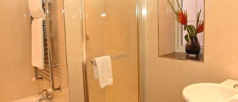 Ein modernes Badezimmer mit einer gläsernen Duschkabine, einem weißen Waschbecken und einem Fenster mit einer Pflanze.
