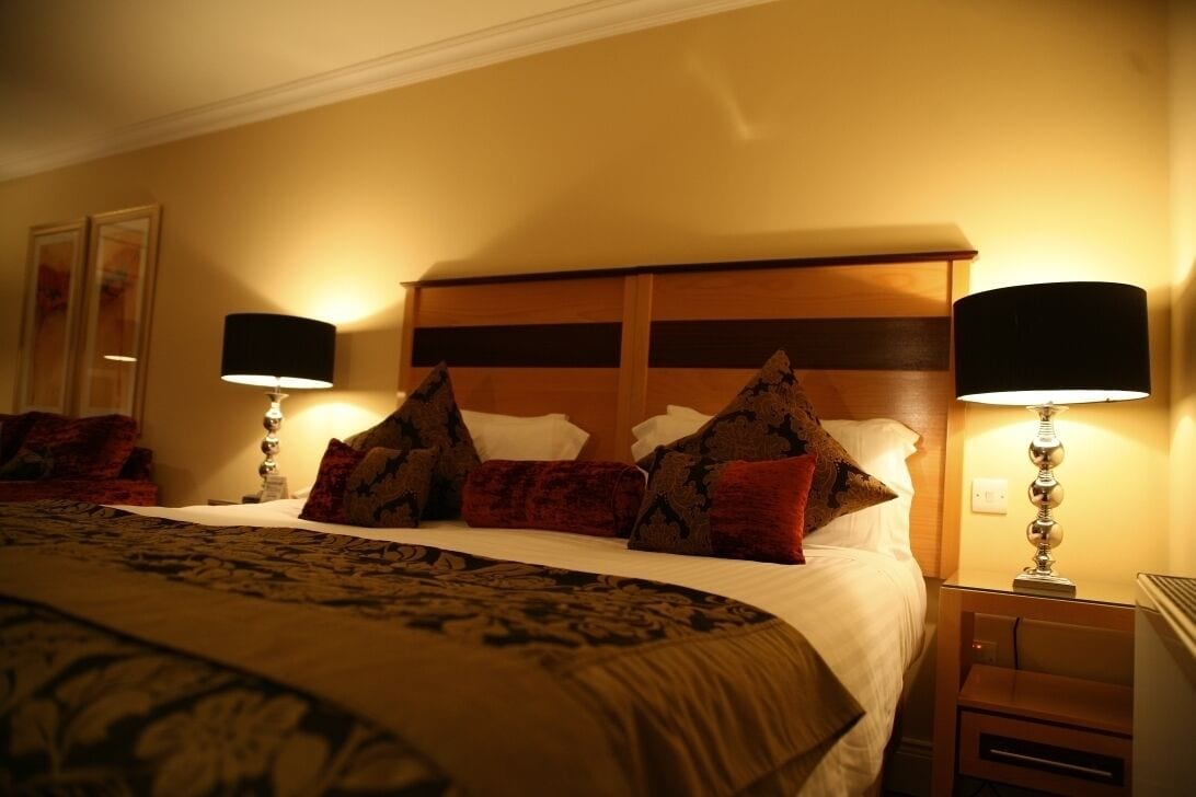 Une chambre d’hôtel avec un grand lit, deux lampes de chevet, une tête de lit en bois et une couvre-lit à motifs.
