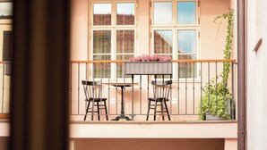 A balcony with a table and two chairs, a potted plant, and a window with a view of buildings. - Hotel Golden Key Prague (Prague)