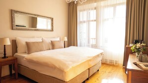 A hotel room with a large bed, two bedside tables with lamps, a mirror, a desk with a vase of flowers, and a window with curtains. - Hotel Golden Key Prague (Prague)