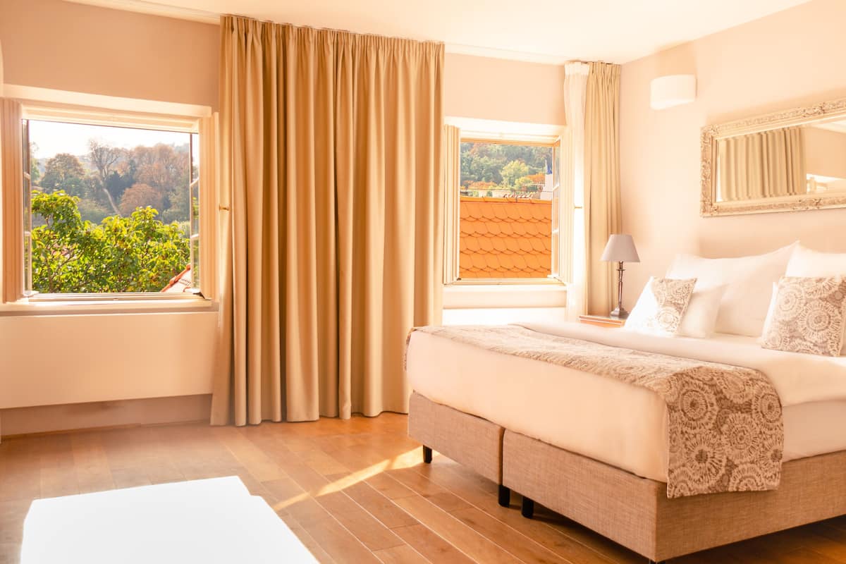 Quarto com uma cama grande, janela com cortinas, mesa de cabeceira, abajur e espelho na parede.