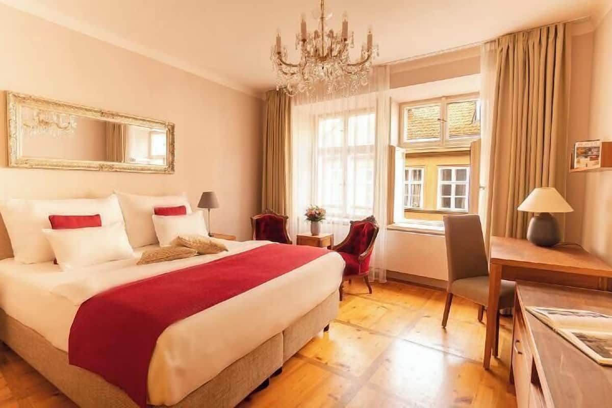 Quarto de hotel com cama grande, lustre, escrivaninha e cadeira.