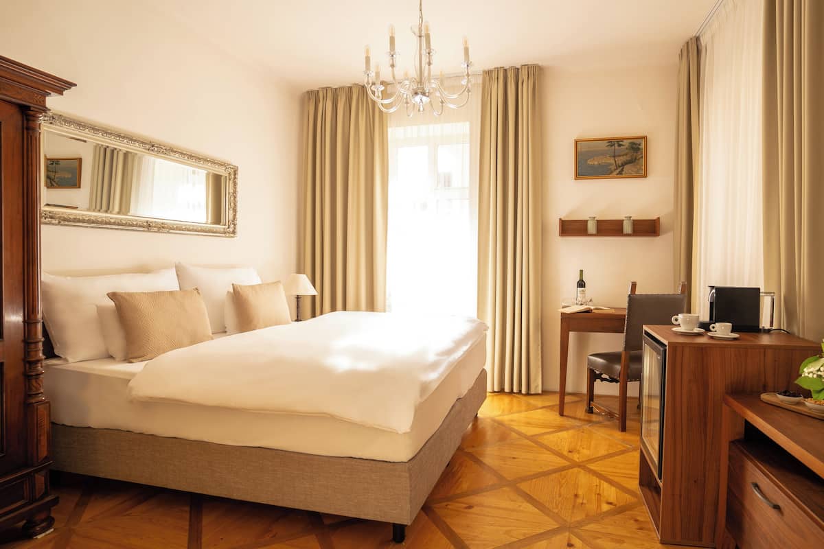 Quarto de hotel com uma cama grande, uma mesa com cadeira, uma TV e uma mesinha com um vaso de flores.
