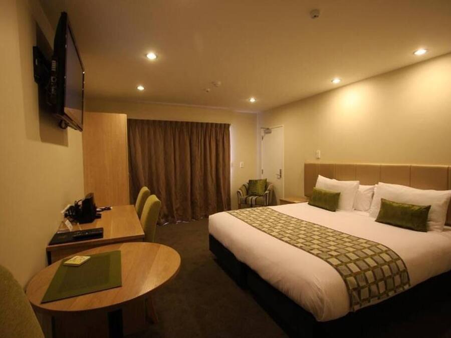 Habitación de hotel con cama, escritorio, silla, televisor y puerta.