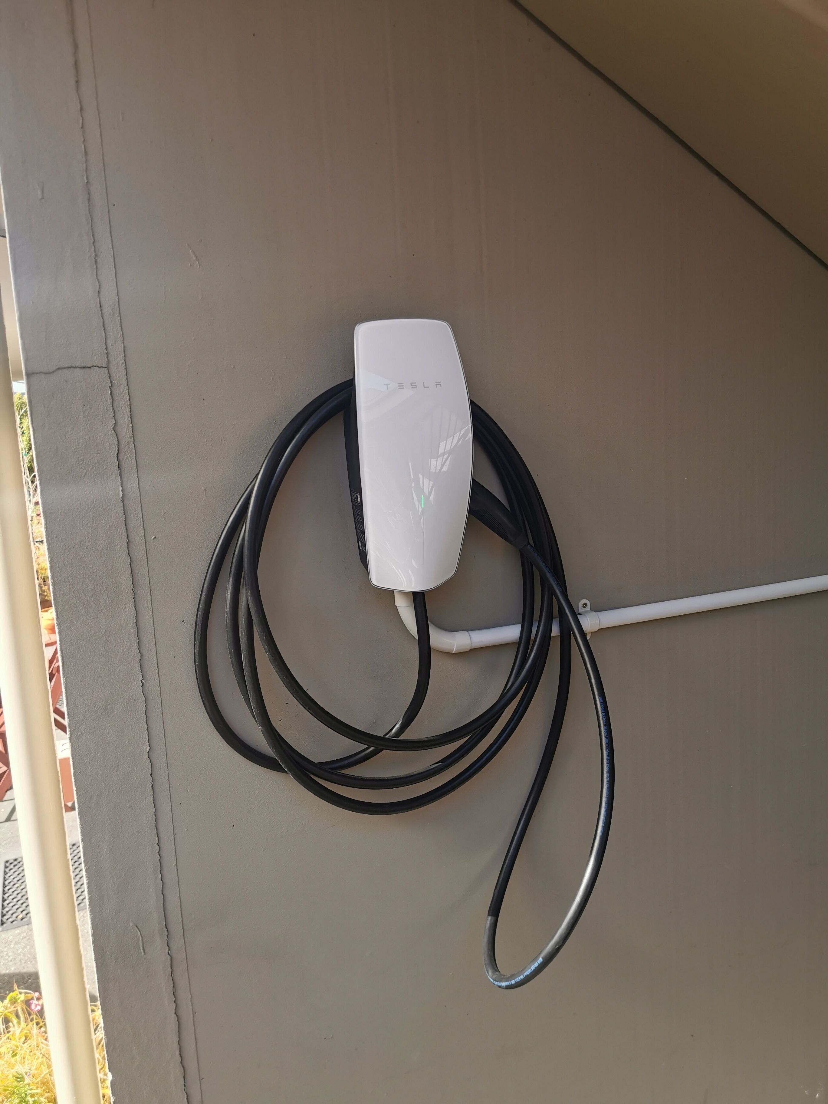 A Tesla charging station with a white box and black cables on a beige wall.
