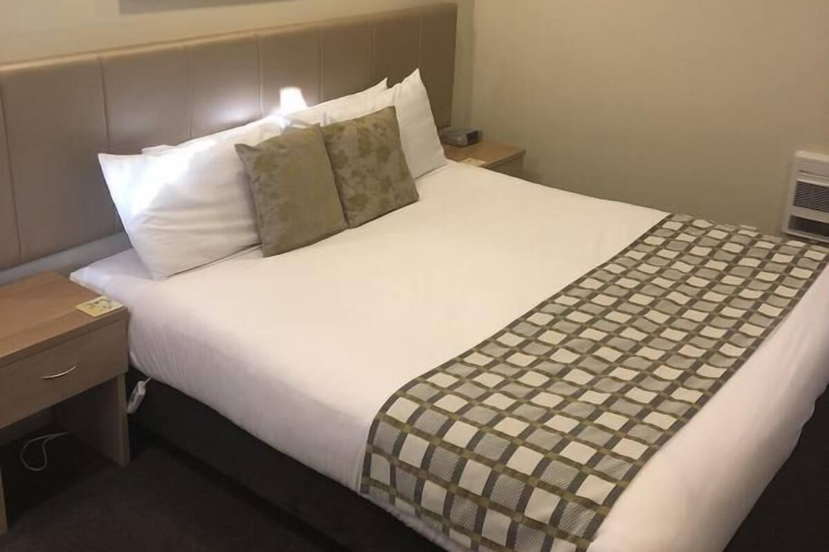A hotel room with a bed, a nightstand, a wall-mounted painting, and a ceiling light.