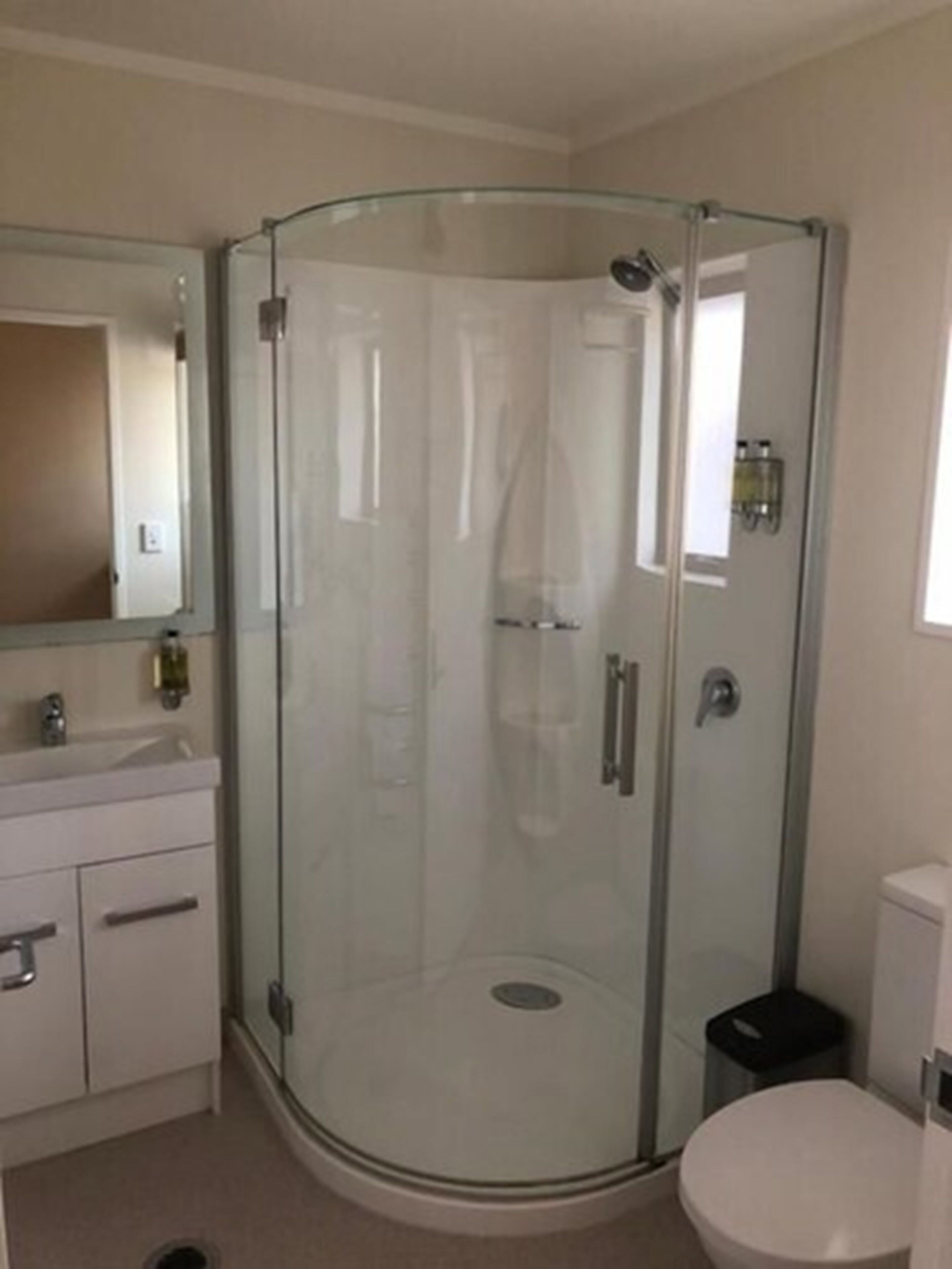 A modern bathroom with a glass-enclosed shower, a white toilet, and a vanity with a mirror.