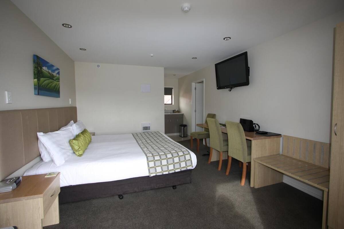 A hotel room with a bed, desk, chair, and a television.