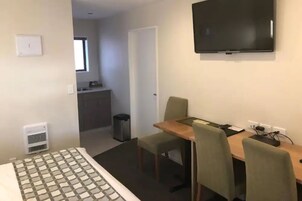 Habitación de hotel con cama, mesa de comedor con sillas, televisor montado en la pared y pequeña cocina.
