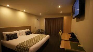 Ein Hotelzimmer mit einem großen Bett, einem Schreibtisch, einem Stuhl, einem an der Wand befestigten Fernseher und einem Fenster mit Vorhängen.