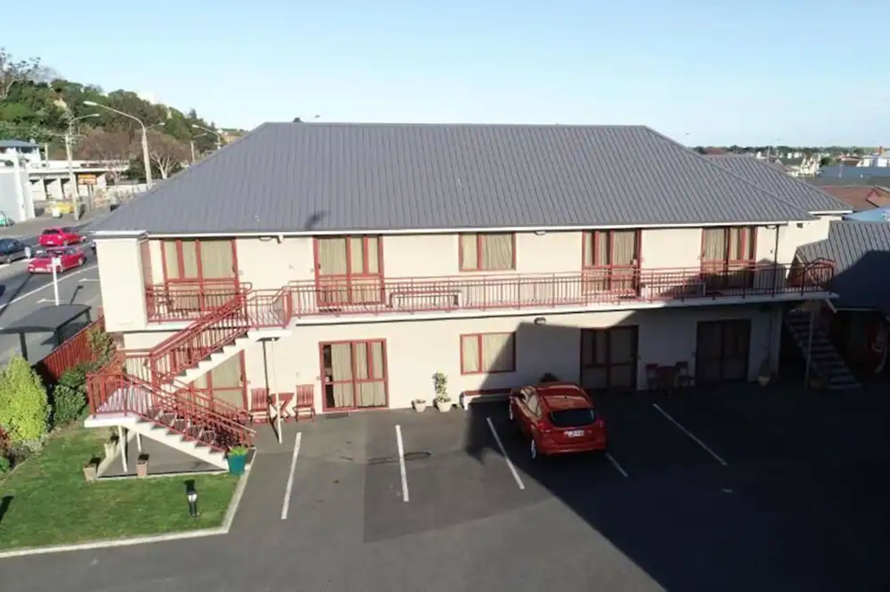 A two-story building with a flat roof, a parking lot, and a red car parked in the lot.