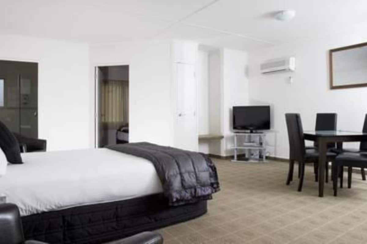 A hotel room with a bed, a desk with a computer, a TV, and a dining area with chairs.