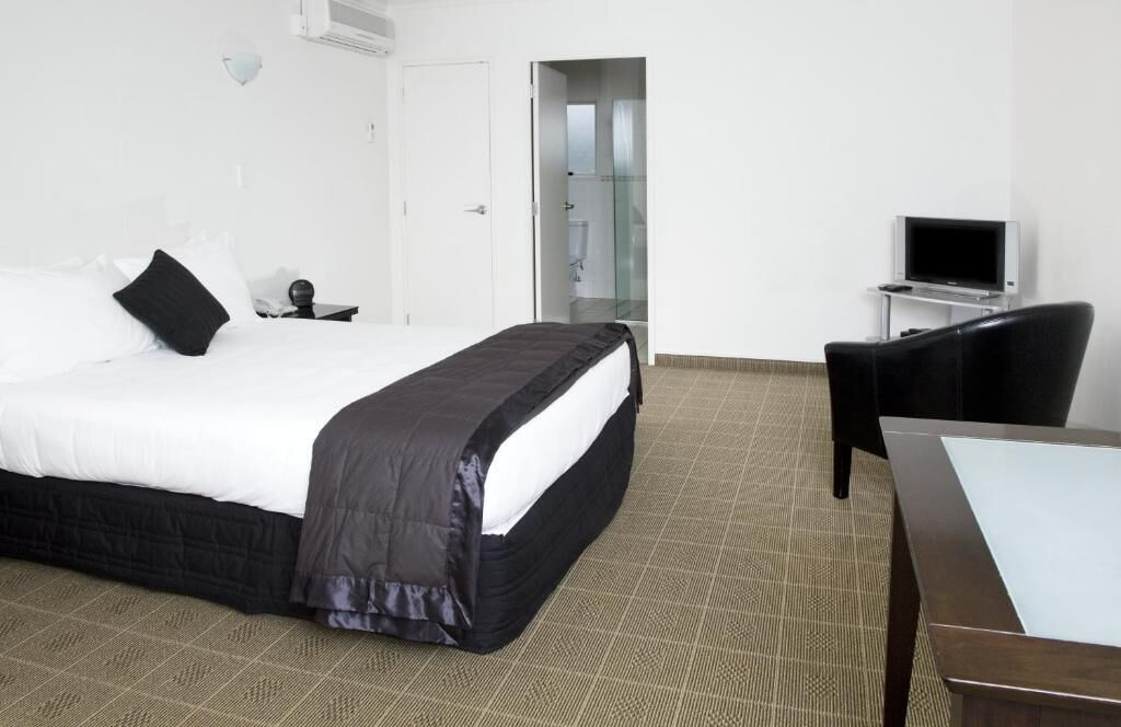 A hotel room with a bed, a desk, a chair, and a television.