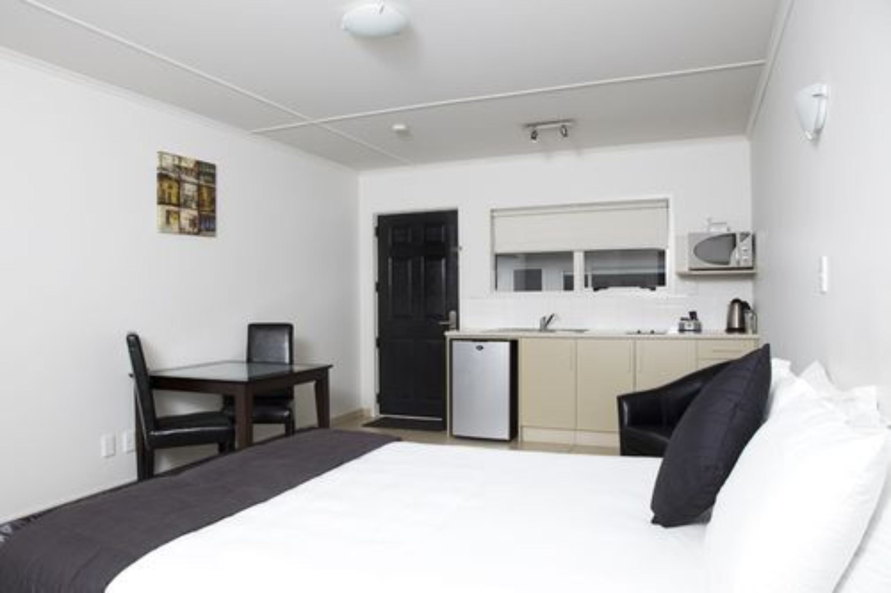A compact hotel room with a bed, a small desk, a chair, a kitchenette, and a microwave.