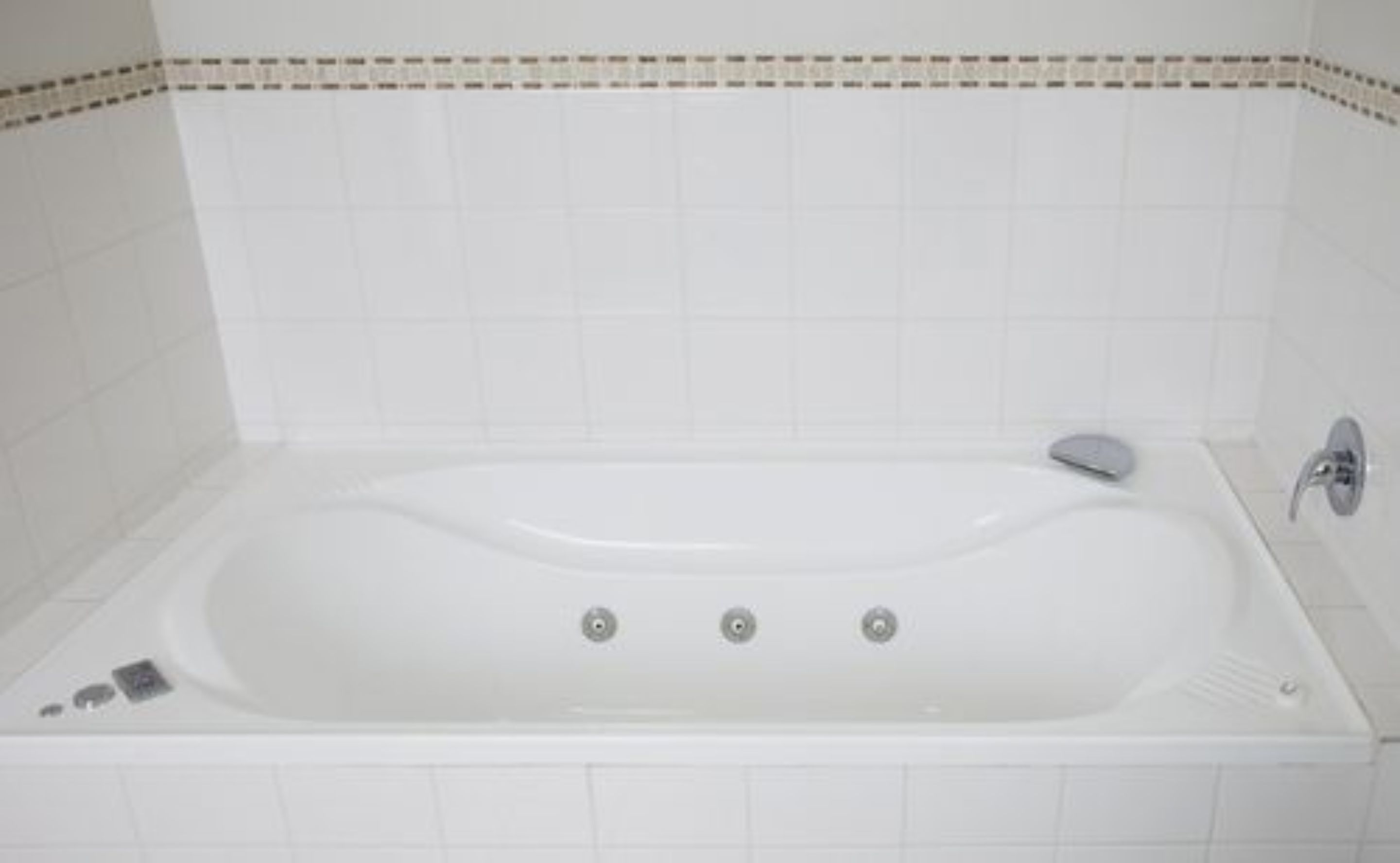 Une baignoire blanche, dotée d’un seul robinet et d’une molette de réglage, est placée contre un mur carrelé orné d’une bordure décorative.
