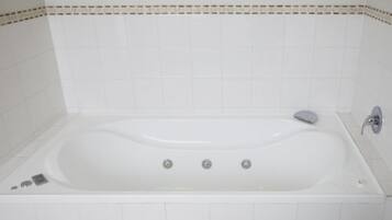 Una bañera blanca con un solo grifo y una perilla, frente a una pared cubierta de azulejos con un detalle decorativo.