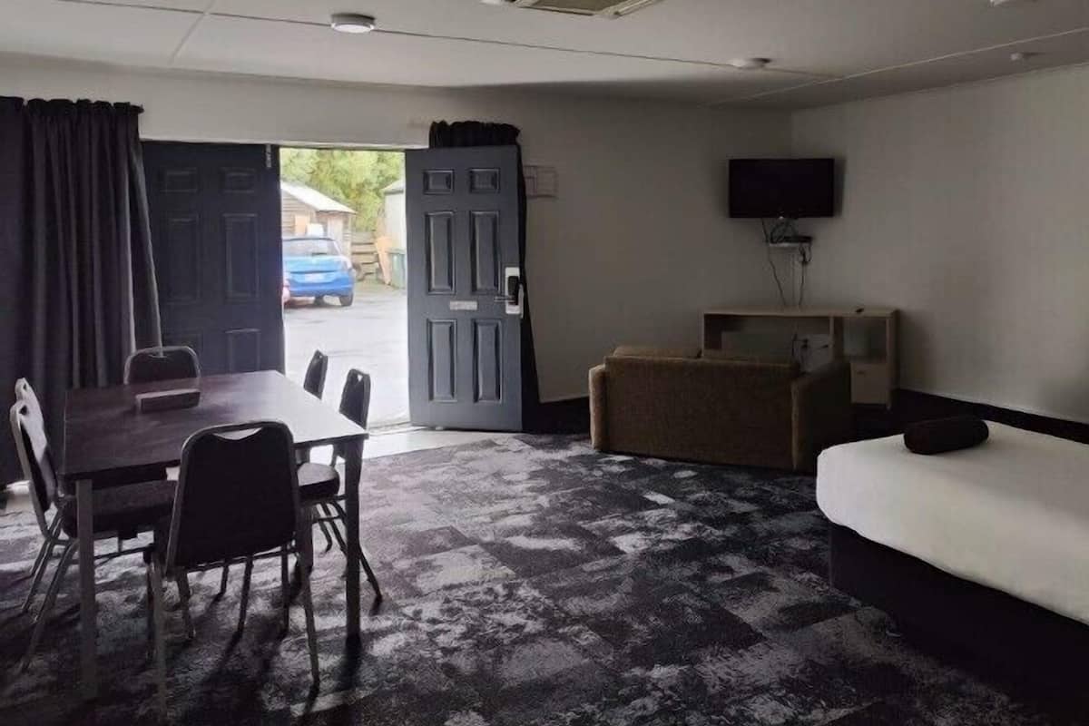 A room with a dining table, chairs, a sofa, a TV, and a door leading outside.