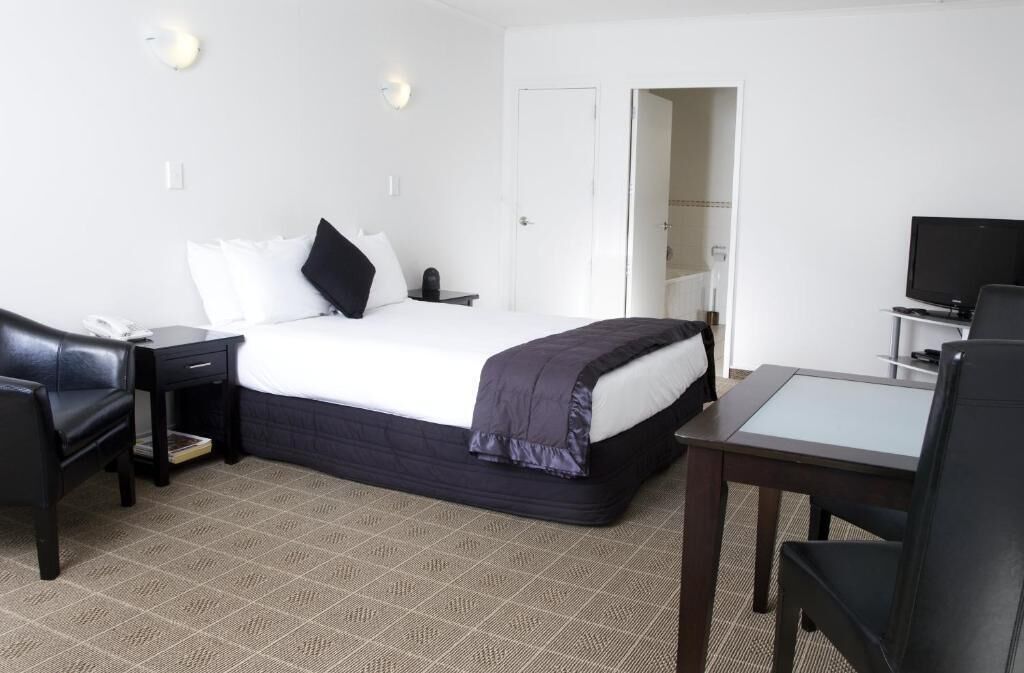 A hotel room with a bed, a desk, a chair, a television, and a wardrobe.
