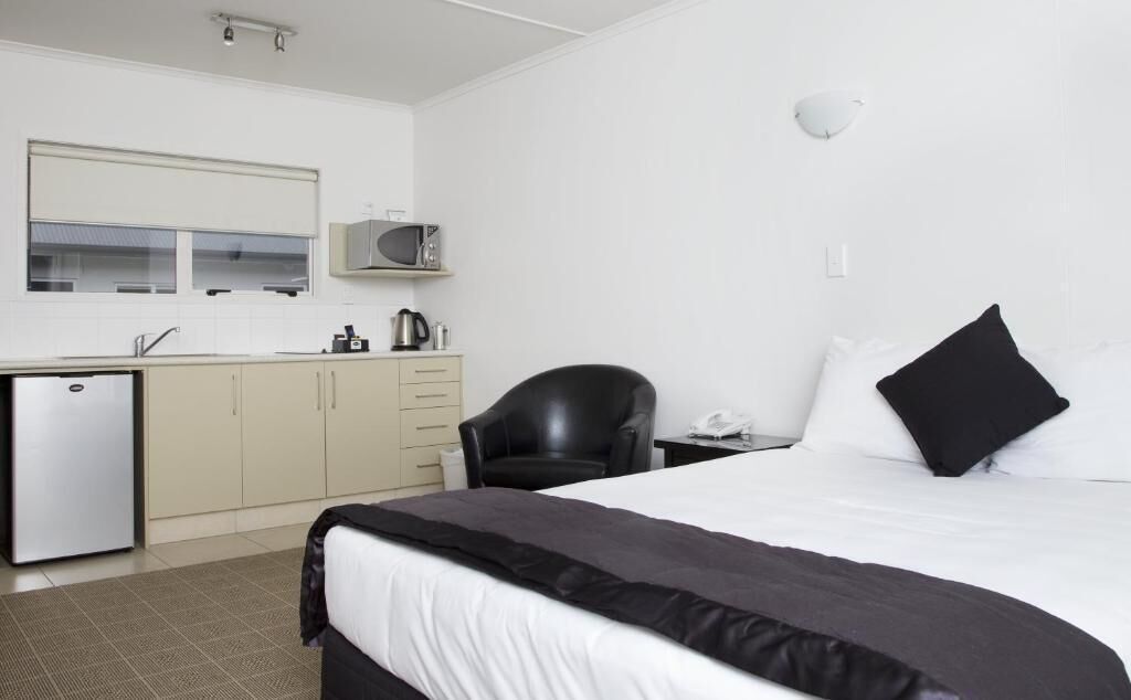 A hotel room with a bed, a desk, a chair, a microwave, a kettle, and a small refrigerator.