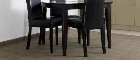 Un coin repas avec une table ronde et quatre chaises, un four à micro-ondes placé au-dessus du comptoir et une fenêtre avec des stores.
