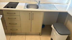 A compact kitchen with a sink, stove, and trash bin. - Hygate Motor Lodge (Hamilton)