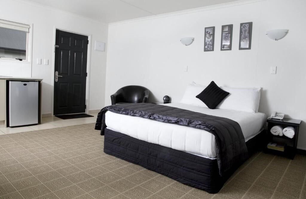 A hotel room with a bed, a desk, a chair, a door, and a small refrigerator.