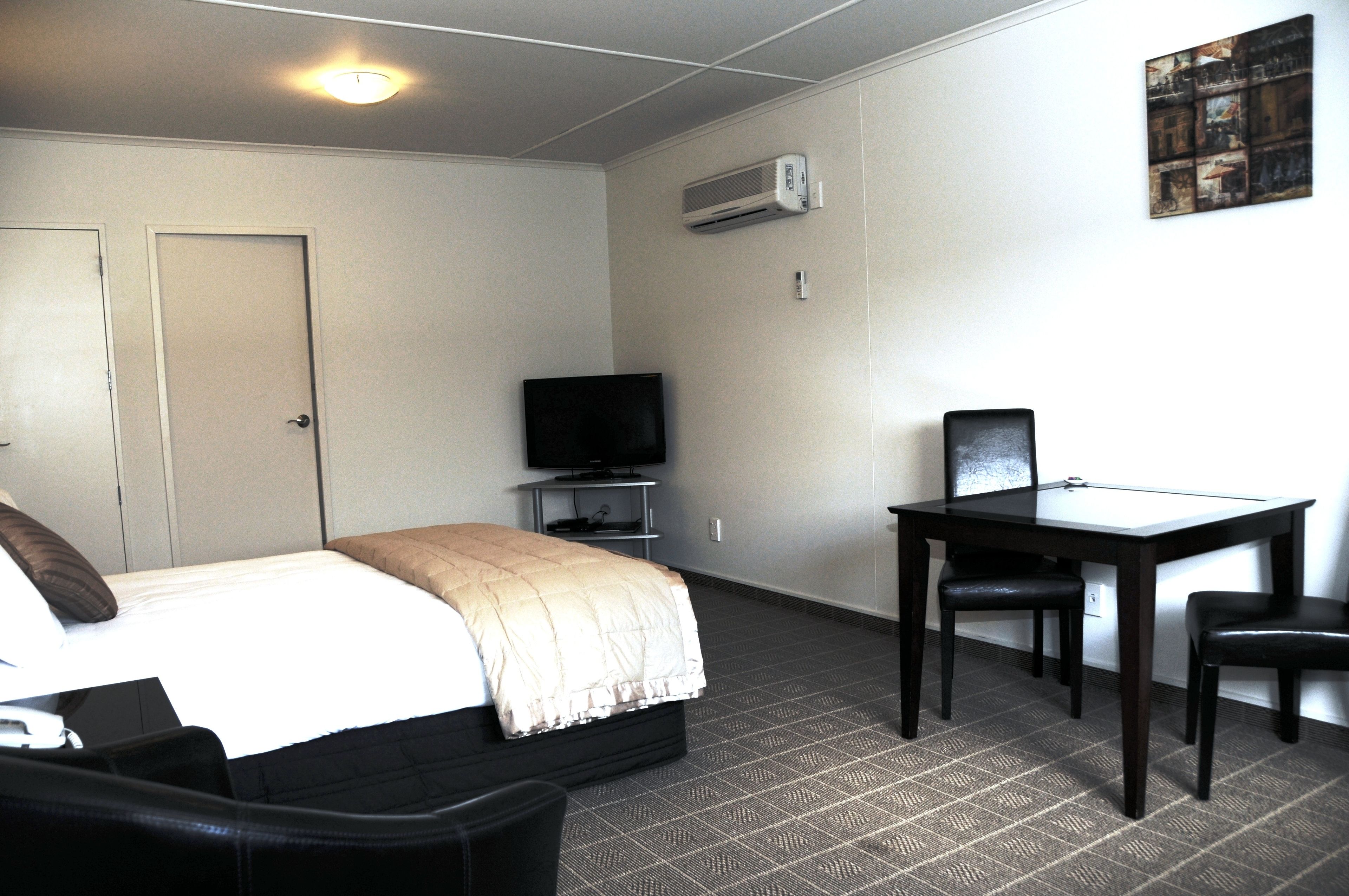 A hotel room with a bed, a desk, a chair, a television, and an air conditioning unit.